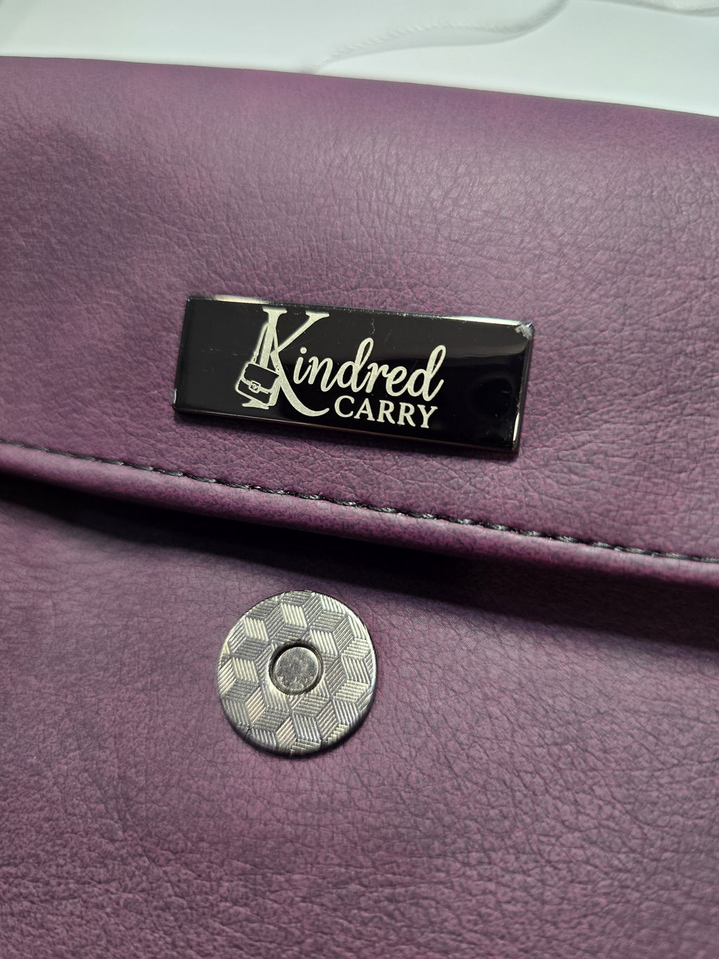Close-up of Kindred Carry label and magnetic snap on the purple Janine clutch
