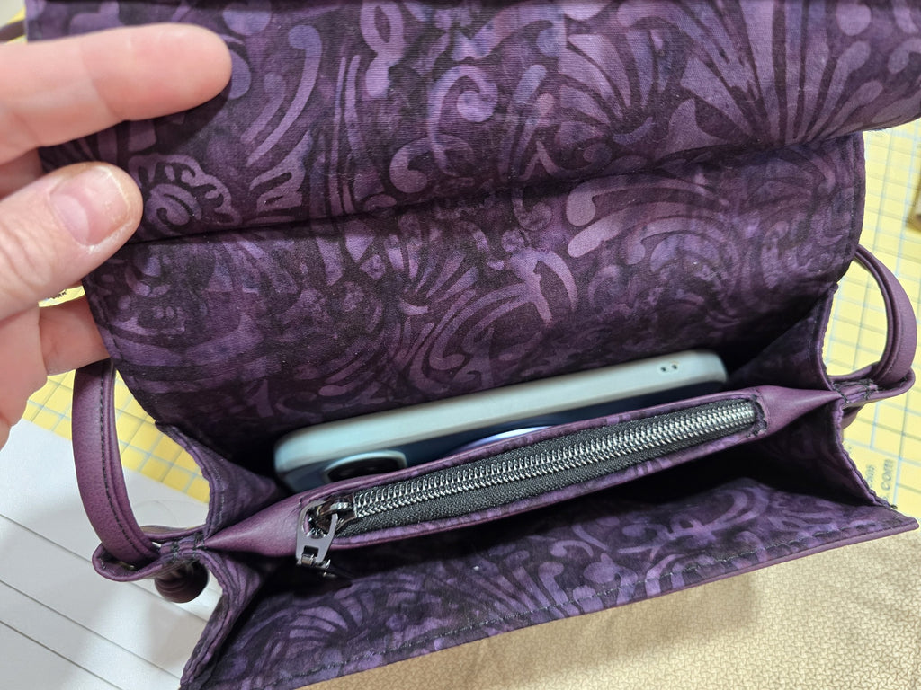 Purple Janine clutch interior shown with a phone for scale and center zip pocket