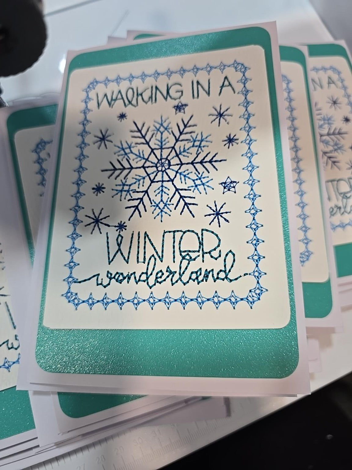 Kindred Carry embroidered Christmas greeting card reading Walking in a Winter Wonderland, with blue snowflakes and shimmery turquoise backing