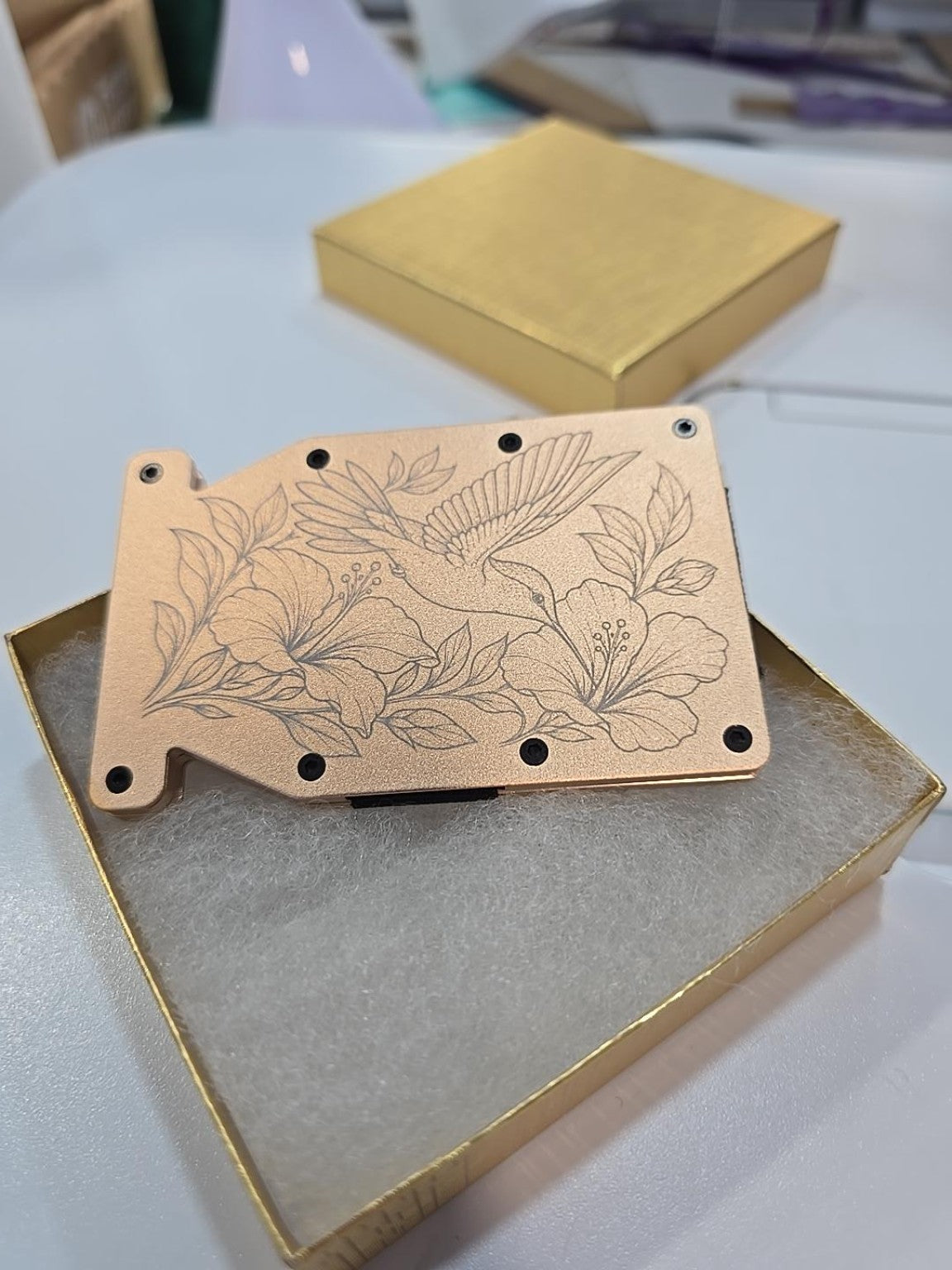 Kindred Carry gold metal Notch RFID wallet engraved with a hummingbird and delicate floral branches, photographed in its gold gift box